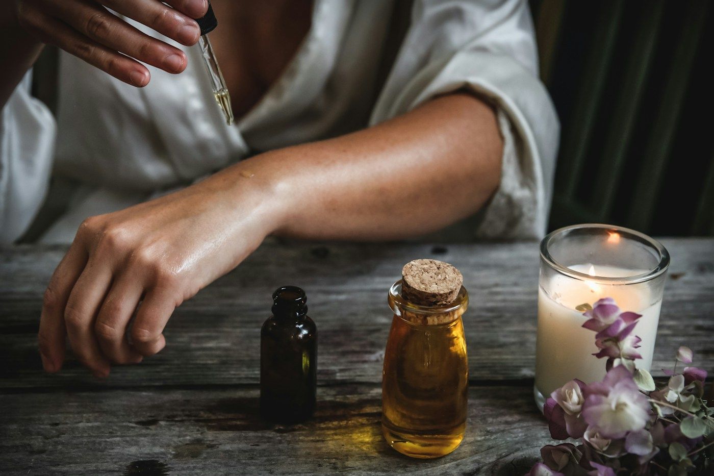 Une femme dépose quelques gouttes d'huile sur sa peau, à côté de flacons en verre ambré.